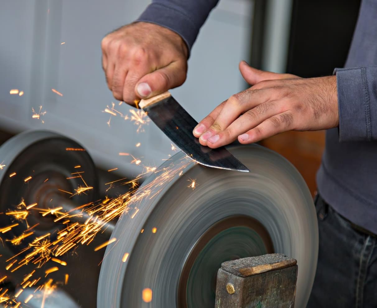 knife being repaired using a stone wheel, sparks flying